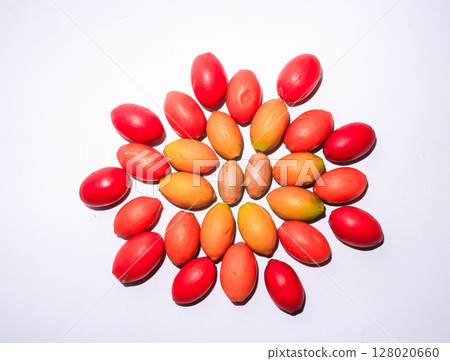 Colorful arrangement of Gnetum gnemon fruits forming a floral pattern on white background. Traditional Indonesian ingredient known as melinjo, used in cooking and emping crackers. Conceptual flat lay  128020660