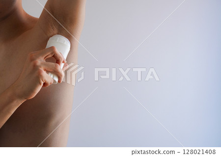 Young man applying antiperspirant deodorant roll-on to his armpits Copy space 128021408