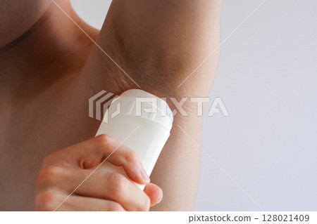 A young man applying antiperspirant deodorant roll-on to his armpits 128021409