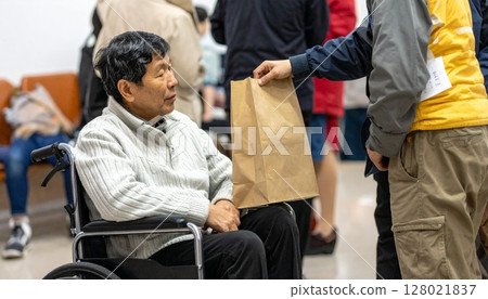 A wheelchair-bound evacuee receives relief supplies at a welfare facility. 128021837