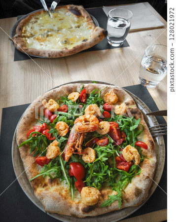 Gourmet pizza topped with succulent shrimp, peppery arugula, and sweet cherry tomatoes at rustic italian eatery in aosta 128021972