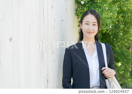 A woman in a suit standing in front of a white fence 128024937