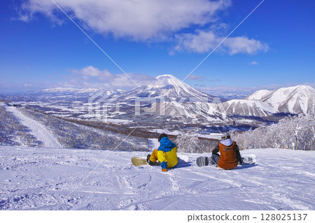 Snowboarders taking a break at Rusutsu Ski Resort in mid-winter, looking at Mount Yotei 128025137