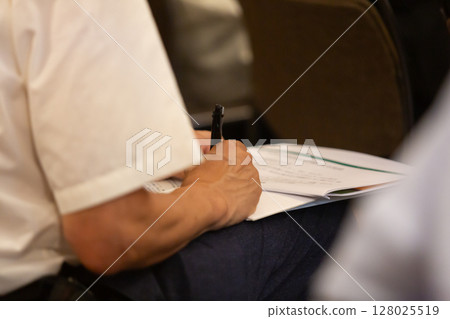 一名男子的手握著筆,在文件上做筆記 一名男子的手握著筆,在文件上做筆記 128025519
