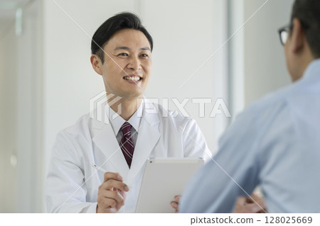 A male doctor holding a tablet and asking questions 128025669