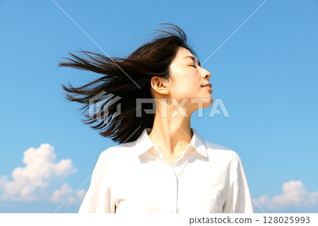 Material with a sense of freedom: cheerful and free. A woman in a white shirt and blue sky. 128025993