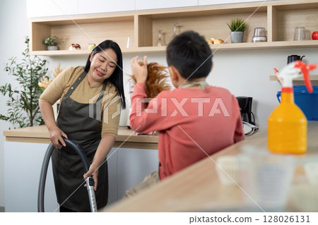 Cleaning Together. Mother vacuuming while her son playfully engages in household chores. Cleaning Together. Mother vacuuming while her son playfully engages in household chores. 128026131
