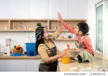 Family Bonding During Cleaning. Mother and son share a high-five while tidying up the kitchen. 128026133