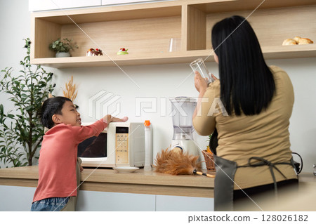 Learning and Helping. Child asking mother for assistance while she prepares a smoothie in the kitchen. Learning and Helping. Child asking mother for assistance while she prepares a smoothie in the kitchen. 128026182