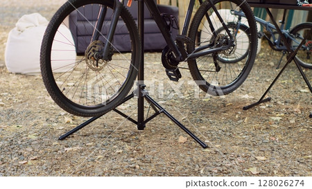 Detailed view of wheels of modern bicycle ready for thorough inspection and repairing as outdoor summer maintenance. Bike placed on repair-stand close-up of tires for fixing in yard. Detailed view of wheels of modern bicycle ready for thorough inspection and repairing as outdoor summer maintenance. Bike placed on repair-stand close-up of tires for fixing in yard. 128026274