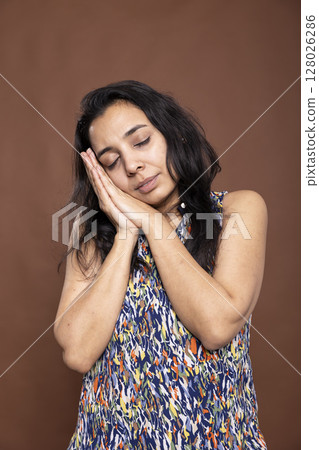 Exhausted woman with her head on hands, appearing sleepy and in need of rest. Female adult posing as if dreaming or napping while standing, expressing peace and tiredness against isolated background. 128026286