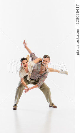 Couple in vintage attire performing energetic dance on white background Couple in vintage attire performing energetic dance on white background 128026417
