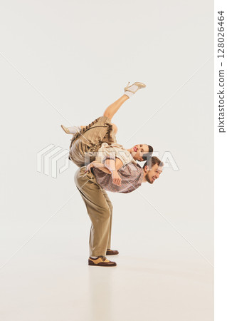 Dynamic retro dance performance with couple in vintage attire and acrobatic pose on neutral backdrop 128026464