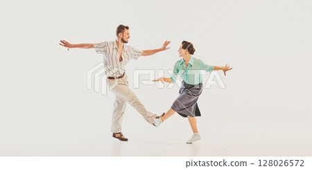 Vintage dance couple performing energetic swing routine in retro attire on white background Vintage dance couple performing energetic swing routine in retro attire on white background 128026572