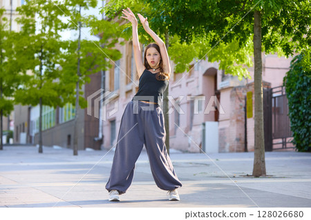 Dancer in relaxed pose on urban street with green trees and pastel buildings in background Dancer in relaxed pose on urban street with green trees and pastel buildings in background 128026680