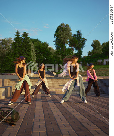 Street dance group performing energetic routine in urban park setting 128026684