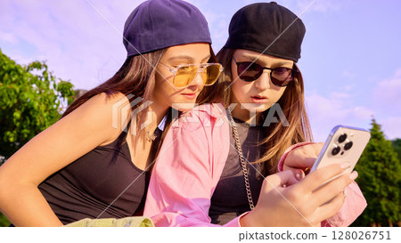 Dance loop. Teen girls in casual dance attire review their dance video on a phone against sunny sky 128026751