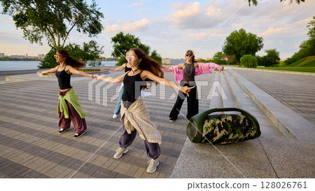 Sound in motion. Group of energetic young women practicing street dance by riverbank Sound in motion. Group of energetic young women practicing street dance by riverbank 128026761