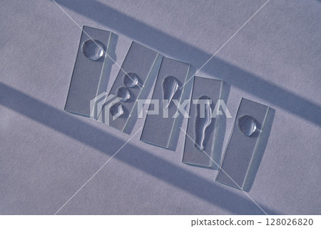 Samples of serum or micellar water on slides on a blue background with streaks of shadows. Samples of serum or micellar water on slides on a blue background with streaks of shadows. 128026820