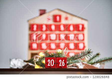 Christmas Advent calendar in the shape of a house with boxes making up the number 2026. 128026848