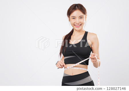 Measure her progress and measure her waist with a gentle smile, this fit and happy woman proudly displays her weight loss journey in a sport and wellness lifestyle. isolated studio white background Measure her progress and measure her waist with a gentle smile, this fit and happy woman proudly displays her weight loss journey in a sport and wellness lifestyle. isolated studio white background 128027146