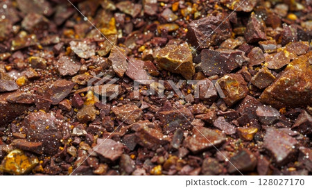 A closeup image of a pile of deep red and brown es with flecks of yellow and green peeking through. The co texture of the es is visible with some pieces appearing to be ground whil 128027170