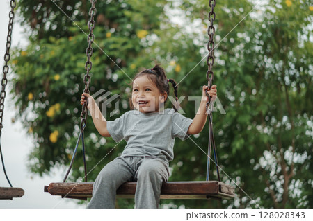 cheerful toddler girl playing on wooden swing at playground cheerful toddler girl playing on wooden swing at playground 128028343