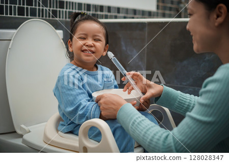 mother making nasal wash for happy toddler girl with syringe and saline. cleaning nose mother making nasal wash for happy toddler girl with syringe and saline. cleaning nose 128028347