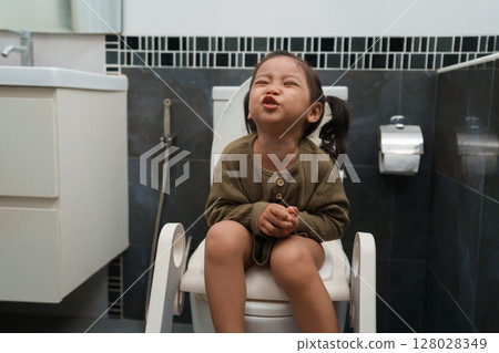 toddler girl sitting on toilet at home and suffering from stomachache and constipation toddler girl sitting on toilet at home and suffering from stomachache and constipation 128028349
