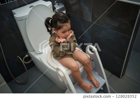 toddler girl sitting on toilet at home and suffering from stomachache and constipation toddler girl sitting on toilet at home and suffering from stomachache and constipation 128028352