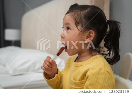 toddler girl takes syrup medicine with syringe by herself. sick child toddler girl takes syrup medicine with syringe by herself. sick child 128028359