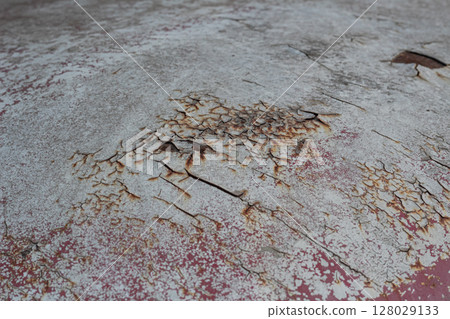 Close-up texture of cracked white paint peeling off a red surface with rust 128029133