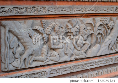 Detailed ancient stone carving artwork showing traditional Balinese mythological scene 128029184