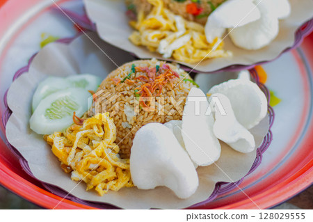 Traditional Indonesian fried rice with kerupuk and cucumber slices being served Traditional Indonesian fried rice with kerupuk and cucumber slices being served 128029555