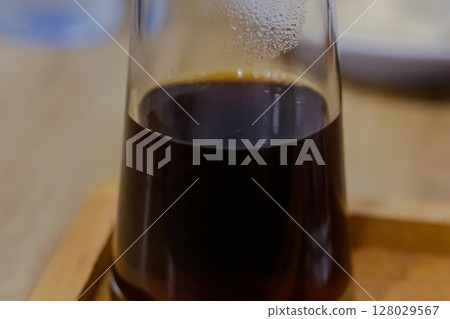 Close-up view of a clear glass containing dark brewed coffee Close-up view of a clear glass containing dark brewed coffee 128029567