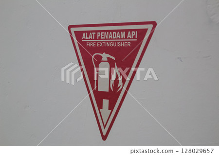 Bright Red Triangular Fire Extinguisher Sign on White Wall Background 128029657