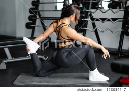 Woman is stretching body in gym. portrait and sport preparation. Young woman is stretching her leg in gym 128034547