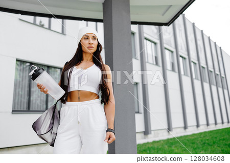 Beautiful woman ready to start her training. Energetic woman is going to gym with sports bag and bottle in hand Beautiful woman ready to start her training. Energetic woman is going to gym with sports bag and bottle in hand 128034608