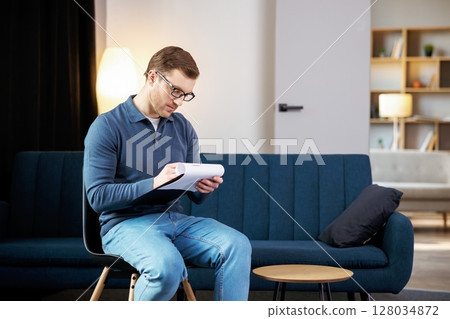 Portrait of happy male psychologist looking at camera and taking notes during therapy session at clinic. Friendly psychotherapist posing and smiling at office 128034872