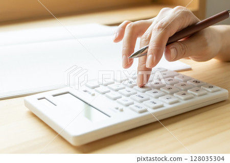 Calculator and notebook in the hands of a woman doing calculations Calculator and notebook in the hands of a woman doing calculations 128035304