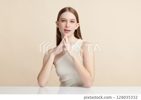 A beautiful young woman with clean, fresh skin against a beige background. Skincare, facial treatment, cosmetology, beauty, and spa. An elegant portrait of an woman. 128035332