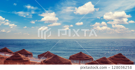 Seascape with beautiful sky and straw umbrellas on the beach on a sunny day. Horizontal banner 128036258