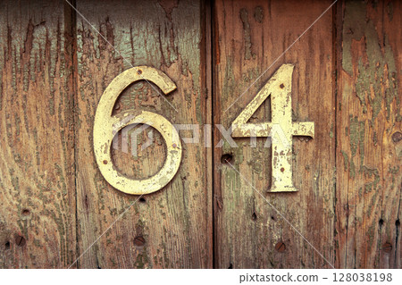 Weathered house number 64 on an old wooden surface 128038198