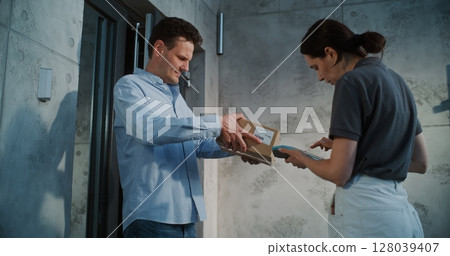Man Taking Package from Female Postal Worker, Paying Contactless Using Smartphone Man Taking Package from Female Postal Worker, Paying Contactless Using Smartphone 128039407