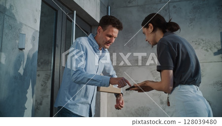 Female Mail Carrier Delivering Small Parcel Box. Businessman Signing POD on Smartphone Female Mail Carrier Delivering Small Parcel Box. Businessman Signing POD on Smartphone 128039480
