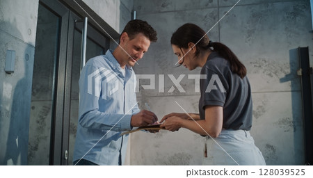 Female Postal Worker Delivering Small Parcel for Recipient in Office, Getting Client's Signature Female Postal Worker Delivering Small Parcel for Recipient in Office, Getting Client's Signature 128039525