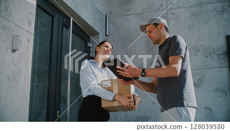 Businesswoman Receiving Her Package from Postal Service Worker, Signing POD on Tablet Computer 128039580