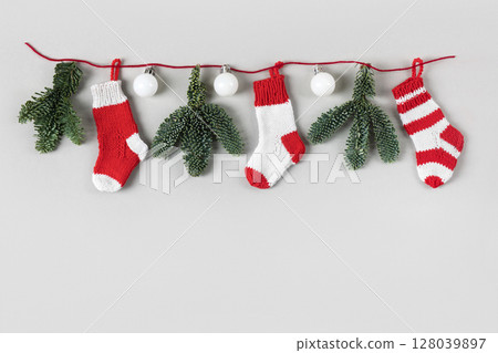 Christmas festive garland of white balls, Christmas tree branches and knitted decorative red socks Santa Claus. Winter knitting creativity Christmas festive garland of white balls, Christmas tree branches and knitted decorative red socks Santa Claus. Winter knitting creativity 128039897