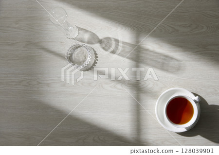 A glass and tea on a wooden table with natural light streaming in through a window. A glass and tea on a wooden table with natural light streaming in through a window. 128039901
