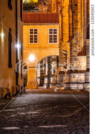 A serene night captures the covered bridge by Saint Vitus Cathedral within Prague Castle, illuminated by street lamps. The cobbled path invites exploration of the historic architecture. A serene night captures the covered bridge by Saint Vitus Cathedral within Prague Castle, illuminated by street lamps. The cobbled path invites exploration of the historic architecture. 128040803